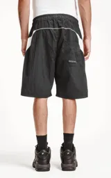 Bermuda negra de textil liviano con calce oversize, cintura elástica con cordón de ajuste y recortes decorativos en blanco. Presenta detalles reflectantes en los bolsillos delanteros y ribetes curvos blancos en la parte inferior.