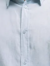 Camisa de manga larga, color blanco, con cuello camisero y botones frontales. El tejido presenta una textura visible de lino.