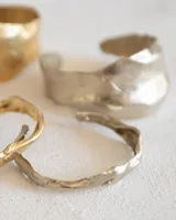 Brazalete rígido abierto de bronce con textura irregular.