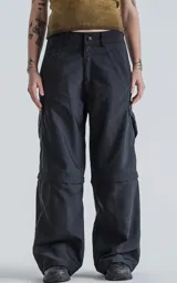 Pantalón negro con corte ancho, bolsillos laterales con solapa y detalle de cierre a la altura de la rodilla para convertirlo en short.