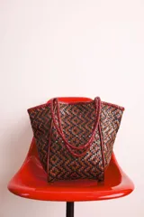 Bolso tote de cuero trenzado en tonos marrón y negro, con asas de cuero trenzado color bordó.