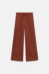 Pantalón palazzo de tiro alto, color beige claro, confeccionado en lino 100%. Presenta cintura ajustable con cordones anudados al frente y pierna ancha.