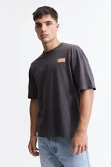 Remera gris oscuro de manga corta con corte boxy, cuello redondo y logo estampado en el pecho.