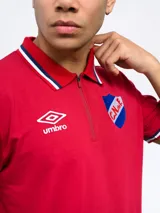 Remera polo azul con cierre, puños y cuello con detalle tricolor. Incluye logo de Umbro y escudo del Club Nacional de Football.
