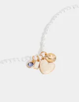Collar corto con perlas blancas irregulares y dijes colgantes dorados: cristal amatista, rectángulo de nácar, corazón de nácar y dije circular con diseño de corazón y rayos.