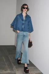 Camisa de denim azul con cuello solapa y mangas amplias tipo kimono. Tiene efecto lavado y cierre frontal con botones ocultos.