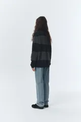 Sweater de punto grueso con diseño de bloques horizontales en tonos de gris y negro jaspeado. Posee cuello polo negro con tres botones de nácar.