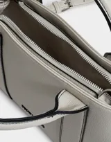 Cartera tipo city color gris claro, con doble asa corta, correa larga regulable y desmontable, cierre superior y tag metálico con el logo de la marca.