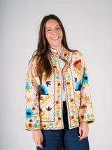 Chaqueta color crema con bordados florales de estilo suzani en tonos azules, rojos, amarillos y verdes.