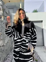Buzo negro con estampado de cebra en blanco, con cuello alto y cierre parcial con botones a presión.