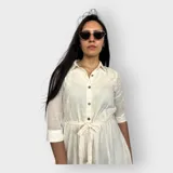 Vestido camisero midi negro con cuello clásico, mangas 3/4 y falda acampanada. Presenta un cinturón de lazo en la cintura y cierre frontal con botones.