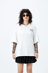 Remera blanca de corte amplio con mangas cortas y estampado con la frase "Unlearn" en el frente y gráfico en la espalda.