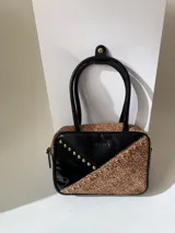Cartera rígida negra de cuero con tachas plateadas y tres combinaciones de cuero diferentes que aportan textura. Tiene herrajes y cierre metálico plateado marca YKK. Cuenta con un asa fina para llevar al hombro o en la mano y una correa larga extra regulable.