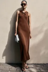 Vestido tobillero marrón sin mangas en punto tupido, con escote en V, sección drapeada con nudo decorativo y detalles cut-out adelante, y falda con leve vuelo.