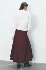 Falda midi color borgoña de tiro alto con tablas en el delantero y cierre frontal cruzado con botones a presión.