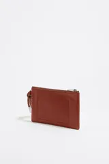 Monedero negro de piel con estructura blanda, asa de mano de cordón extraíble, logo metálico, acabados metálicos plateados, bolsillo interior y cierre con cremallera. Interior con etiqueta de tejido BIMBA Y LOLA.