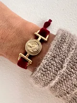 Pulsera de aleación de metales con baño de oro y banda de terciopelo elástico en color burdeos.