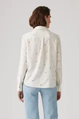 Camisa de lino color blanco hueso con estampado floral en tonos marrones. Tiene cuello clásico, cierre frontal con botones y mangas largas con puños abotonados.