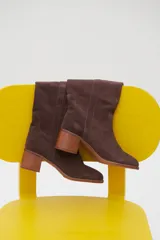 Botas de caña media color marrón de gamuza, con puntera fina y taco cuadrado de madera. Presenta pespuntes verticales en el frente y laterales.