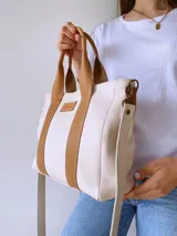 Bolso tipo tote de lona color crudo con detalles en cuero color marrón. Tiene doble asa corta de mano y correa larga de hombro.