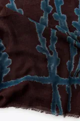 Pañuelo rectangular de lana color marrón con estampado abstracto en azul. Tiene terminaciones deshilachadas.