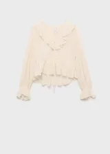 Blusa color crema con estampado de lunares, escote en V con volantes y lazos, mangas largas abullonadas con puños elásticos y corte peplum.