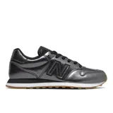 Championes New Balance modelo 500 (GW500WR1) para mujer, con acabado metalizado gris oscuro/plata, cordones negros y detalles en textura de piel de serpiente en el talón. La suela es blanca con una capa inferior de goma color caramelo.