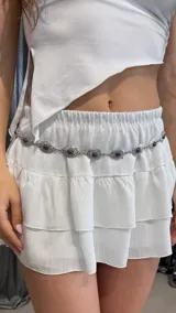 Cinturón plateado tipo cadena con eslabones circulares con centro de piedra negra.