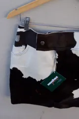 Falda corta confeccionada a mano en cuero ovino con estampado de vaca en blanco y negro. Presenta bolsillos delanteros y traseros, y un diseño de tiro medio con cierre de botón.