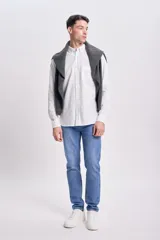 Camisa blanca de lino, de corte clásico, con cuello abotonado, manga larga con puños abotonados y bolsillo en el pecho.