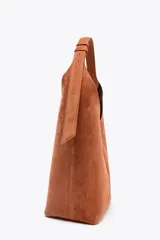 Bolso tipo saca color marrón de piel, con asa al hombro y cierre imantado. Incluye cartera interior con cierre de cremallera metálica.