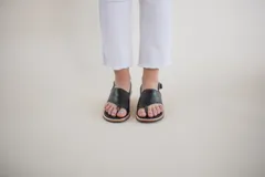 Sandalias de cuero negro con tira entre los dedos, talón descubierto y hebilla lateral.