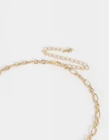 Collar corto dorado con cadena de eslabones y dijes colgantes: taxi amarillo, manzana y pretzel dorados.