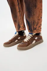 Zapatillas urbanas marrones de cuero con detalles en color crema, cordones off-white y suela color caramelo.