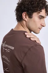 Remera de manga corta color marrón oscuro con cuello redondo y un pequeño texto bordado en blanco en el pecho.