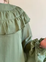Blusa verde con cuello alto con volados, mangas largas con puños elásticos y transparencias.