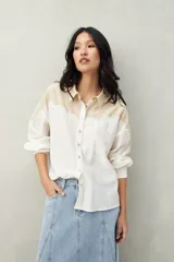 Camisa de lino color crudo y beige, con diseño bicolor y recorte ondulado en el canesú. De silueta relajada, cuenta con mangas amplias y puños camiseros. Se completa con botones de nácar.