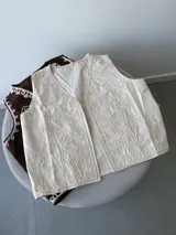 Chaleco sin mangas color beige claro, con bordados florales en relieve y abertura frontal.