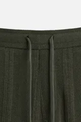 Pantalón verde oscuro con textura de rayas verticales, corte relaxed fit, cintura elástica ajustable con cordón, bolsillos delanteros y bolsillo trasero de parche.