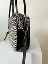 Cartera rígida negra de cuero con tachas plateadas y tres combinaciones de cuero diferentes que aportan textura. Tiene herrajes y cierre metálico plateado marca YKK. Cuenta con un asa fina para llevar al hombro o en la mano y una correa larga extra regulable.