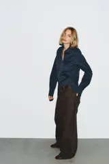 Jeans de mezclilla color marrón oscuro, tiro bajo, corte baggy barrel (ancho y holgado con caída recta). Presenta cinco bolsillos y cierre frontal con cremallera y botón metálico.