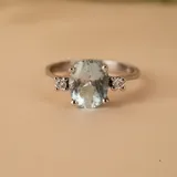 Anillo solitario de oro blanco 18k con aguamarina central ovalada y brillantes laterales engarzados en 4 puntas. El ancho de la banda es de 2,4 mm.
