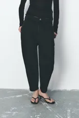 Pantalón de jean negro con efecto lavado, tiro alto, corte carrot fit, cintura elástica en la parte trasera, bolsillos delanteros y traseros, cierre frontal con cremallera y botón metálico.