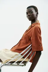 Camisa de lino color celeste claro, con cuello solapa, escote pico, manga corta con vuelta y dos bolsillos de plastrón en el delantero. Cierre frontal con botones.