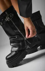 Botas de caña media color marrón oscuro, de cuero vegano, con suela track y cierre lateral con cremallera. Presentan hebillas decorativas y tirador trasero.