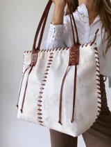 Bolso tipo tote bag de cuero color crudo con detalles de costuras y tiras de cuero marrón.