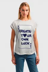 Remera blanca con estampado de una carta de póker con el texto 'Create your own luck'.