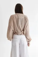 Camisa tostada en voile de algodón con cuello a la base y mangas balloon. Cierre frontal con lazos en la misma tela y tablas en el frente y en el medio en la espalda.