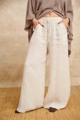 Pantalón palazzo color crudo, de lino, con cintura elastizada y bolsillos laterales desflecados.