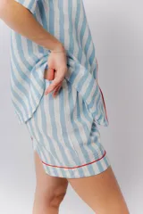 Pijama de lino a rayas verticales blancas y celestes, con vivos rojos. Incluye camisa de manga corta abotonada y short con elástico en la cintura.